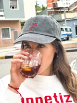 Gorro de béisbol de color gris oscuro (obsidian) con efecto lavado, confeccionado en algodón. Presenta un bordado frontal de un ají picante rojo y verde.