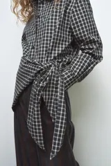 Camisa oversize de algodón con estampado de cuadros, cuello solapa, manga larga con puños y cierre frontal con botones. Presenta un detalle de pañuelo integrado en el mismo tejido que se anuda en la parte frontal.