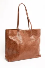 Cartera tipo tote bag color marrón whisky, con diseño trenzado y doble asa larga de hombro. Presenta una pequeña placa metálica dorada con el logo de la marca en el frente.