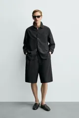 Bermuda relaxed fit de color negro, confeccionada en tejido fluido con viscosa y modal. Presenta cintura elástica ajustable con cordón, pliegues en el delantero, bolsillos frontales y bolsillos traseros de vivo.