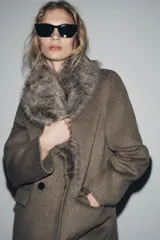 Chaqueta de corte recto confeccionada en mezcla de lana, color marrón topo. Presenta un cuello de solapa amplio con aplicación de pelo sintético desmontable, cierre frontal cruzado con botones y bolsillos laterales con solapa.