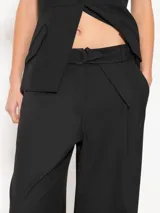 Pantalón negro de lanita viscosa, corte wide leg con gran caída y movimiento. Acceso mediante cierre metálico, gancho pantalonero y botón interno. Incluye lazo en cintura con media caña marcaria de níquel.