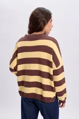 Buzo tejido oversize de manga larga con diseño de rayas horizontales en color amarillo y marrón, cuello redondo y hombros caídos.