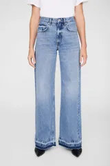 Jean de corte baggy y pierna ancha, confeccionado en denim de algodón sin elasticidad con lavado vintage medio. Presenta tiro alto, cierre con cremallera, diseño clásico de cinco bolsillos y ruedo al corte con efecto desgastado.