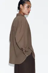 Camisa oversize de algodón con cuello solapa, manga larga y cierre frontal con botones. Presenta un bolsillo de plastrón en el frente y un diseño de corte amplio con ruedo redondeado.