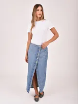 Falda larga de denim color gris oscuro, con diseño cruzado frontal (wrap) que se ajusta con botones plateados, creando una abertura pronunciada.