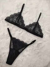 Conjunto de lencería de encaje negro, compuesto por un soutiene triangular de tirantes finos y una bombacha colaless ajustable con tiras laterales.