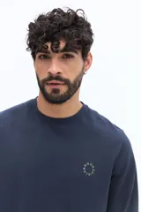 Remera de manga larga color azul marino, con escote redondo y un pequeño logo circular bordado en el pecho.