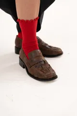 Mocasín de cuero color chocolate con acabado texturizado y diseño enrejillado en la capellada. Presenta horma cuadrada, taco bajo y suela de goma.