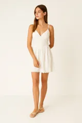 Vestido corto de algodón con diseño broderie, escote profundo y tirantes finos regulables. Presenta un corte holgado con falda acampanada y terminaciones festoneadas en el escote y el ruedo.