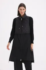 Chaleco largo negro de diseño combinado, con parte superior en matelassé y parte inferior de tela lisa. Presenta cuello alto con cordones ajustables y cierre frontal completo.