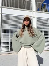 Poleron de tejido suave color verde, con cuello alto, corte holgado y mangas amplias con aberturas laterales en el ruedo.