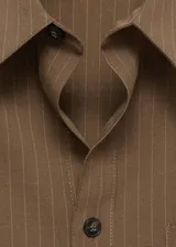 Camisa oversize de corte recto con diseño de raya diplomática, cuello camisero, cierre frontal de botones y bolsillo de parche en el pecho.