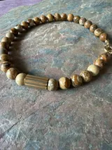 Collar de piedras naturales en tonos tierra, con detalle de tubo dorado en un lateral y cierre marinero dorado.