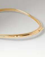 Brazalete rígido de oro de diseño ondulado y sutil, adornado con pequeñas circonitas blancas distribuidas a lo largo de la pieza.