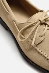 Zapato tipo náutico de cuero color beige, con cordones de cuero y suela plana de goma negra.