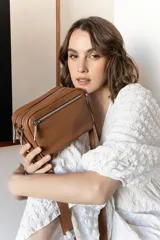 Bandolera rectangular de cuero color nude, con correa larga ajustable y doble cierre superior con cremallera metálica plateada.