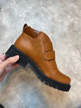 Borcegos de cuero color marrón con textura tipo reptil, caña baja, ajuste con dos correas con hebilla y suela track color negro.