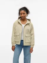 Campera corta tipo parka color beige, con capucha ajustable, cierre frontal y dos bolsillos delanteros con solapa. Presenta puños elásticos y un diseño funcional y versátil.