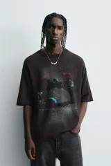 Camiseta negra de algodón con corte boxy fit y cuello redondo. Presenta un estampado gráfico desgastado con temática espacial o celestial en tonos azules y blancos, y texto en la parte superior e inferior.