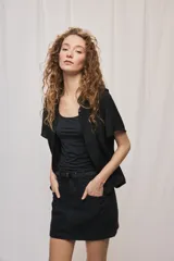 Camisa negra de manga corta, silueta amplia y tejido liviano con textura. Presenta cuello mao, cierre frontal con botones y diseño fluido.