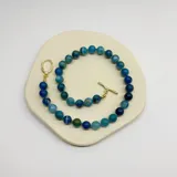 Collar elaborado con bolitas de ágata azul de 10 mm de diámetro, con separadores de hilo color turquesa. El cierre es un broche tipo T (toggle) de metal con baño de oro.