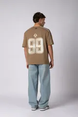 Remera de algodón color blanco con corte regular, cuello redondo y mangas cortas. Presenta detalles de líneas finas negras en los hombros y estampado gráfico frontal con tipografía y logotipos en color negro.