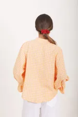 Blusa de diseño cuadrillé en tonos beige y verde claro, de corte amplio y mangas largas abullonadas con puños elastizados con volados. Cuenta con cuello mao y una abertura frontal parcial con botones.