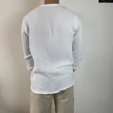 Camisa de manga larga confeccionada en muselina de algodón, con cuello mao y cierre frontal de tres botones. Presenta una textura arrugada característica del tejido y puños con opción de arremangar.