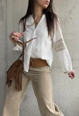 Camisa blanca de calce relajado y tejido liviano, con escote en V y delicados detalles bordados geométricos en tonos tostados en las mangas abullonadas y puños.
