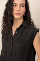 Conjunto compuesto por una blusa sin mangas con cuello camisero, bolsillos frontales y cierre de botones, y un pantalón largo de corte recto y holgado, ambos confeccionados en tejido texturizado de color marrón.
