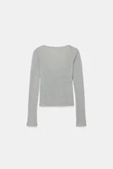 Chaqueta de punto color beige con escote en pico y manga larga, que incluye un top interior integrado con detalle de encaje a tono. Cierre frontal mediante botones.