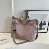 Bolso tipo tote color gris claro, con doble asa de mano y correa larga regulable. Tiene dos bolsillos laterales y un bolsillo frontal.