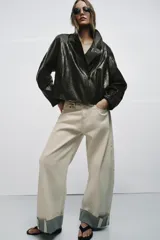 Chaqueta de corte amplio estilo biker en tejido efecto piel de color verde oscuro, con cuello alto envolvente, cierre frontal asimétrico de cremallera metálica, bolsillos ocultos en costura y forro interior.