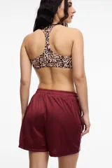 Short deportivo color bordó, confeccionado en tela satinada de poliéster. Presenta una franja lateral blanca, bolsillos laterales y cintura elastizada.