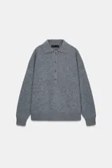 Sweater de punto liso color gris melange, con cuello polo, manga larga y cierre frontal con botones. Presenta puños y ruedo acanalados.