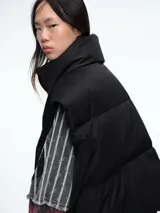 Chaleco puffer de corte holgado y diseño acolchado, con cuello alto, cierre frontal oculto y bolsillos laterales. Ideal para superponer sobre otras prendas.