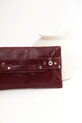 Sobre de cuero negro con solapa, cierre magnético y muñequera con tachas plateadas.