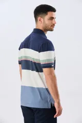 Remera polo de manga corta con diseño de franjas horizontales en tonos azul, beige, verde y terracota. Presenta cuello camisero con cierre frontal de dos botones y un pequeño bordado en el pecho.