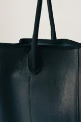 Bolso tipo tote de gamuza color marrón con detalles de bordes y asas en cuero negro.