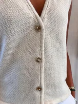 Chaleco de punto color crudo con escote en V y botones dorados.