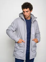 Parka larga gris con capucha, cierre frontal con cremallera y botones a presión, múltiples bolsillos y logo de Umbro en el pecho.