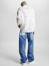 Camisa blanca de popelina de puro algodón con estampado de banderas náuticas y logos de Tommy Jeans bordados. Corte clásico, cuello abotonado, puños con botón y bajo redondeado.