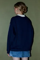 Buzo azul marino con cuello polo blanco y cierre parcial. Presenta un estampado frontal con la palabra "BALANCE" en blanco y "and focus" debajo, junto con un logo circular en el pecho. Tiene rayas blancas en las mangas.