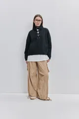 Pantalón cargo negro de corte relajado y pierna ancha con bolsillos laterales con solapa, cintura con doble broche y cierres metálicos en los tobillos.
