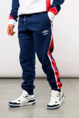 Pantalón deportivo tipo jogging de la marca Umbro, en color azul marino con bandas laterales en rojo y blanco. Cuenta con el escudo del Club Nacional de Football en el muslo derecho y el logo de Umbro en el izquierdo, además de cintura elástica ajustable con cordón y puños en los tobillos.