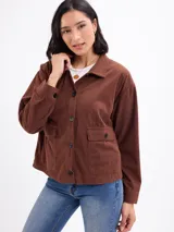 Campera de pana color beige, con cuello camisero, cierre frontal de botones oscuros, mangas largas con puños abotonados y dos bolsillos frontales con solapa.