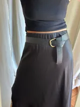 Cinturón negro con hebilla dorada en forma de media luna y textura símil cuero de reptil.