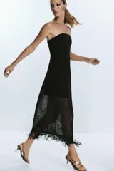 Vestido midi negro de tejido calado con hilo metalizado, escote recto palabra de honor, forro interior y flecos en el ruedo. Cierre lateral con cremallera oculta.