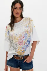 Remera de algodón blanca de corte oversize y silueta recta, con escote redondo, hombros caídos y mangas cortas amplias. Presenta una estampa frontal con diseño paisley en tonos rojo, azul, amarillo y gris.